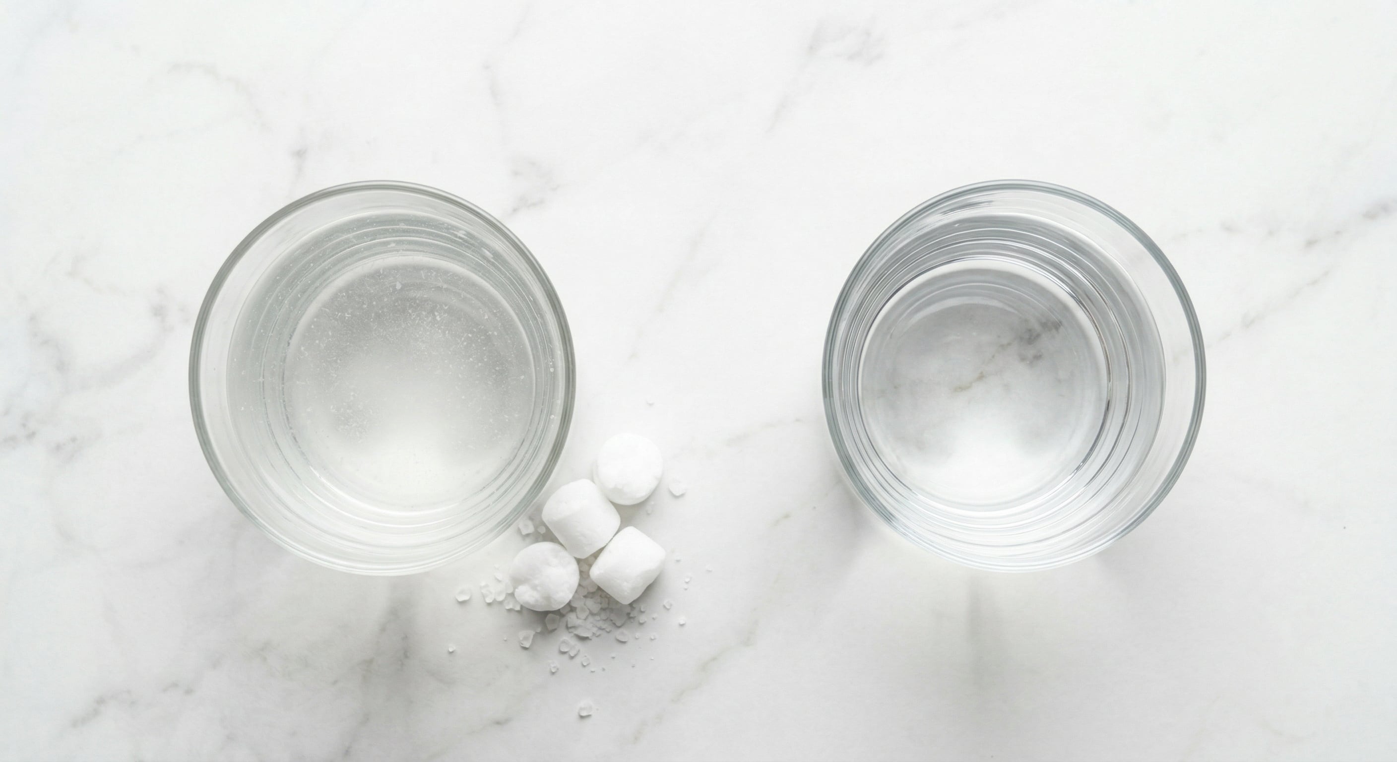 Two glasses of water comparison - hard water with mineral deposits versus purified RO water